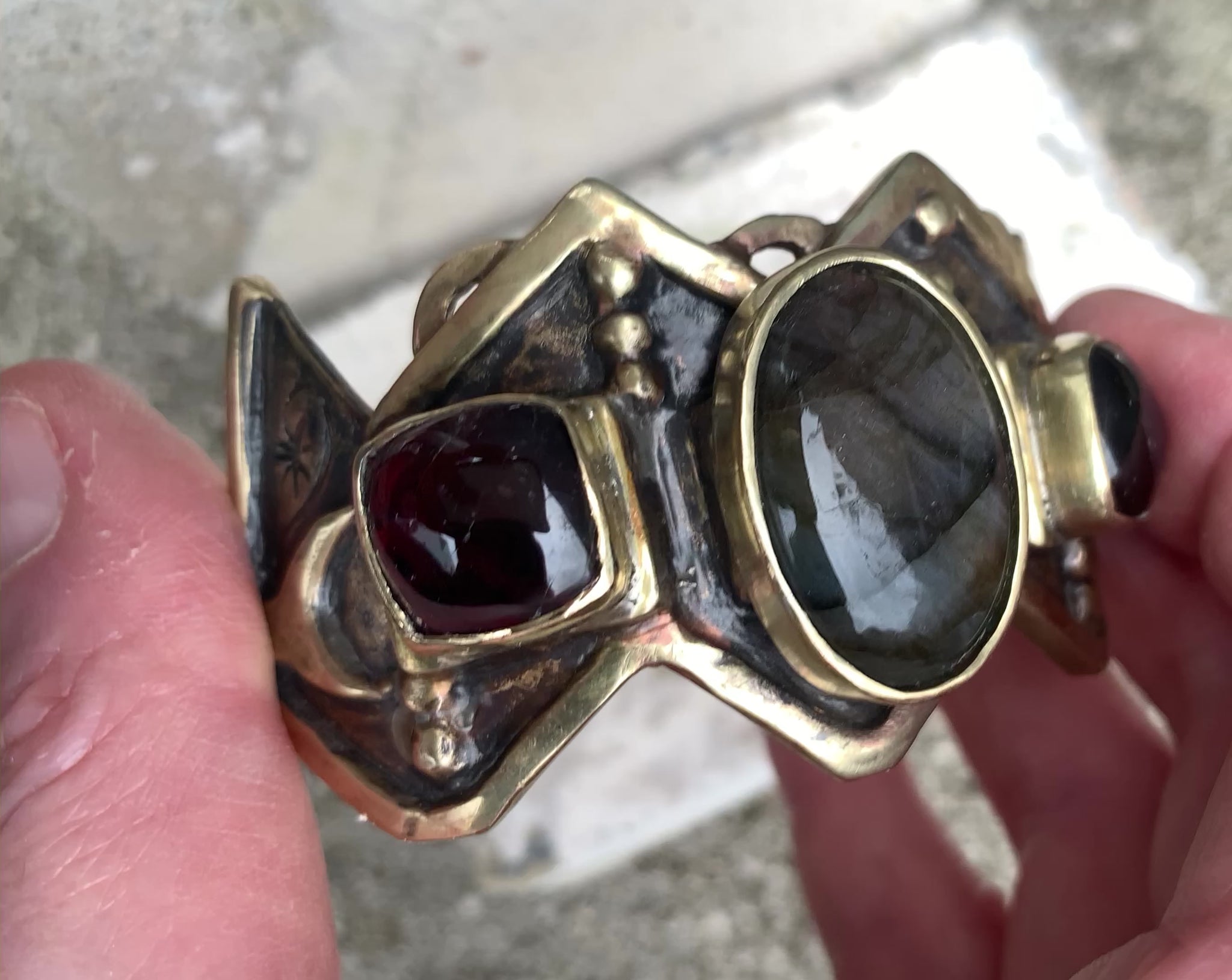 Bracelet de fonte en laiton, sertis d'une labradorite et de deux grenats. Le haut est découpé en W, symbole berbère de la fourdre, et le bas en M (symbole de fécondité). Vidéo de présentation.