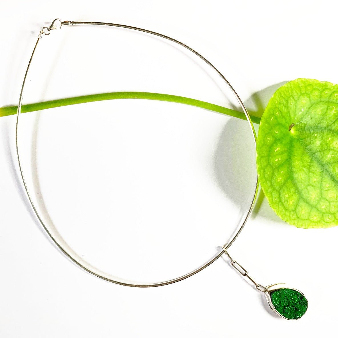 Et si vous accrochiez un fragment de roche à votre cou ? Ce collier en argent de 40 cm présente au centre une uvarovite druzy sertie clos pour la protéger des chocs. Sa forme druzy fait qu'elle est recouverte de minuscules inclusions brillants au soleil. Ce pendentif est long de 5 cm, accroché par des chaînons rectangles en argent. Vue de face.