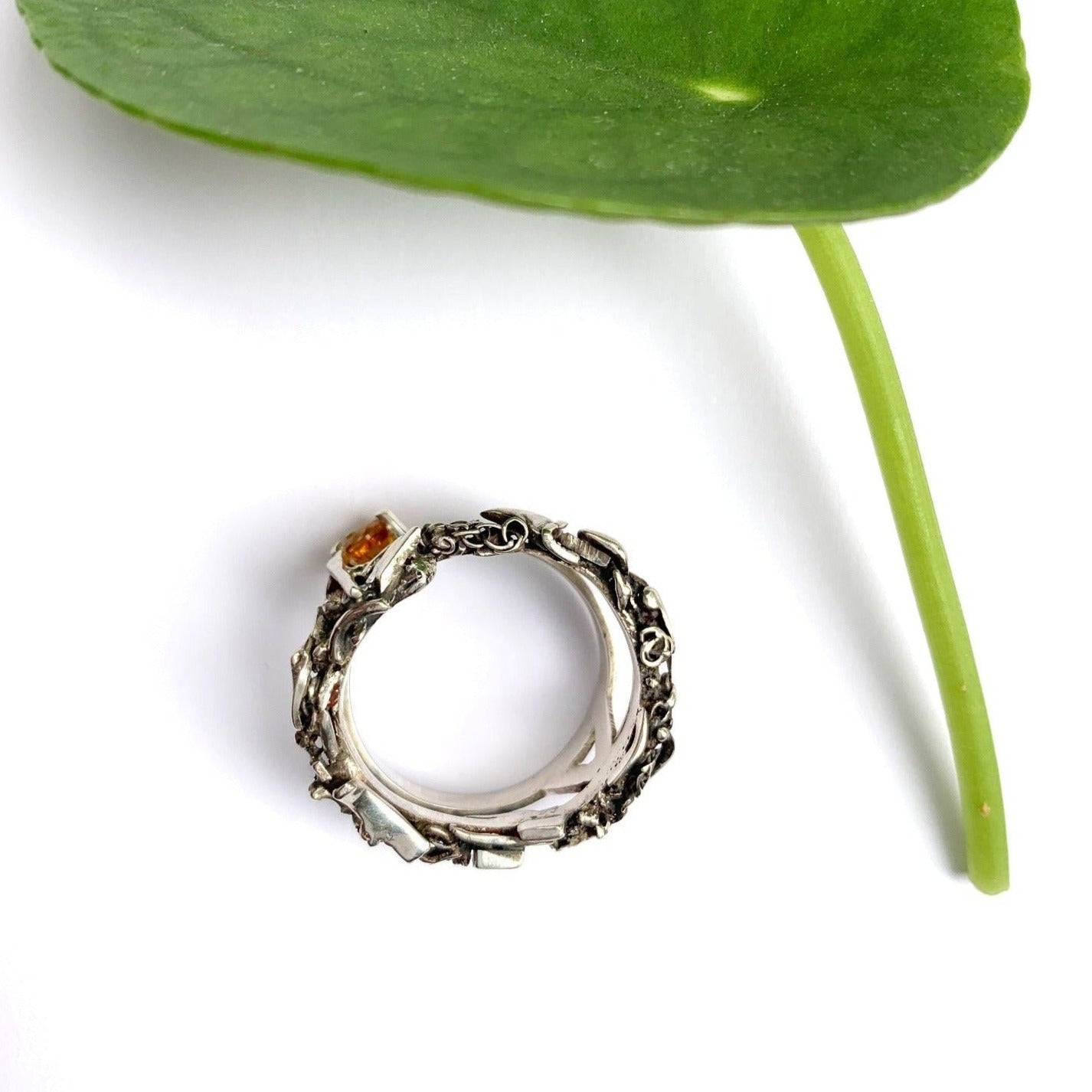 Inspirée par les couronnes de fleurs de Tahiti, cette bague évoque le Lei, symbole de l'Aloha hawaïen. Elle se compose de deux joncs : un petit en taille 62 avec une citrine de 5 mm, porté côté main, et un jonc plus large pour le pouce, constitué de morceaux d'argent travaillés. Les deux joncs sont reliés par un pont en forme de tige de plante, Vue de de dessus coté jonc façonné.