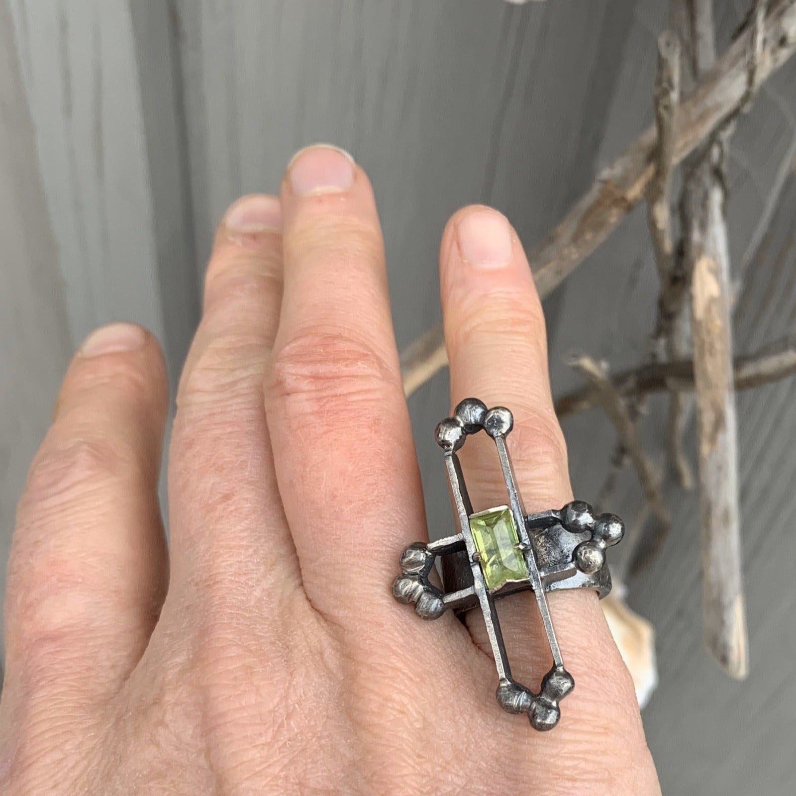 Bague en argent massive et texturé, sur le doigt un soleil amazigh soit une croix avec son centre déportée au milieu o se trouve sertie une sphène de Madagascar d'un vert translucide. A chaque extrémité de cette croix évidée en 3D un système de triangle composé de 3 billes soudées entre elles. Vue portée.